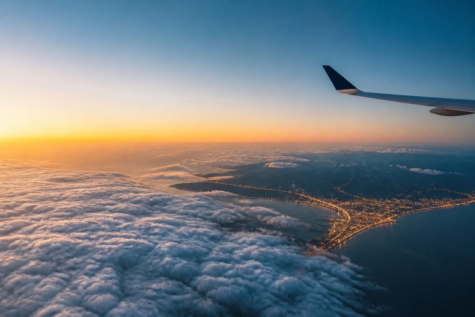 Airplane wing above clouds and a coastline at sunrise